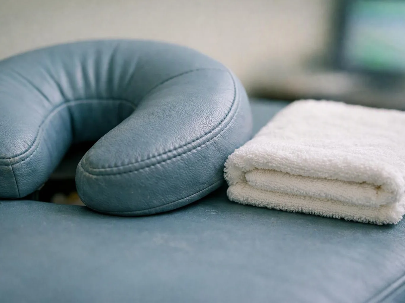 A blue neck pillow sits beside a folded white towel on a cushioned surface