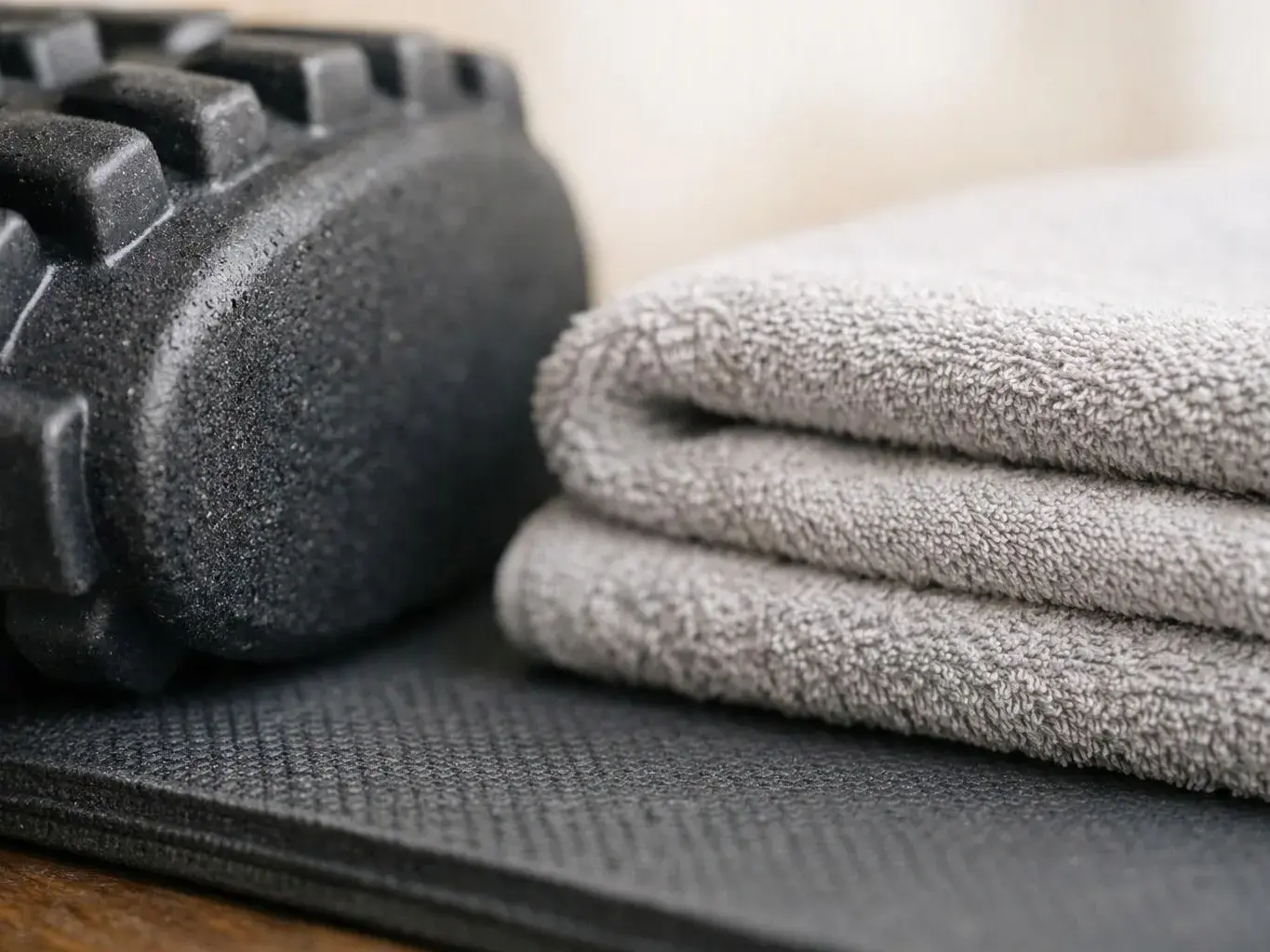 Folded gray towels sit beside a black foam roller on a textured exercise mat